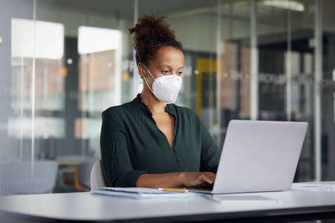 Porträt einer Geschäftsfrau mit Schutzmaske, die an einem Laptop am Schalter arbeitet, lizenzfreies Stockfoto