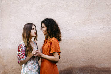 Portrait of two young women holding hands looking at each other - TCEF00661