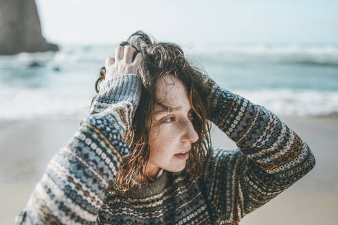 Junge Frau mit Händen im Haar, die wegschaut, während sie am Praia da Ursa steht, Lisboa, Portugal - FVSF00345