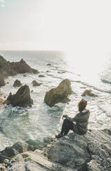 Young woman sitting on rock formation while looking at sea, Praia da Ursa, Lisboa, Portugal - FVSF00350