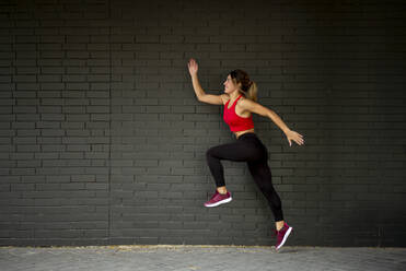 Mid adult woman wearing sports clothing while running against brick wall - OCMF01243