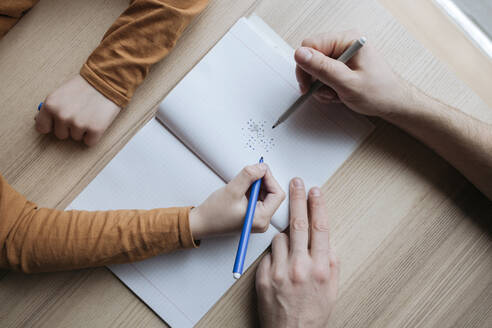 Top view of father and son scribbling into notebook on table - EYAF01067