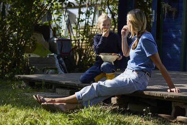 Mutter und Tochter essen Erdbeeren auf der Terrasse im Garten - MCF00844