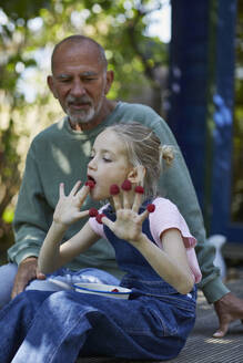 Grandfather and granddaughter eating raspberries on terrace in garden - MCF00854