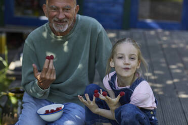 Großvater und Enkelin essen Himbeeren auf der Terrasse im Garten - MCF00855