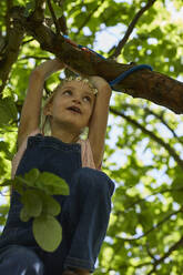 Mädchen mit Gänseblümchenkranz klettert auf einen Baum - MCF00887