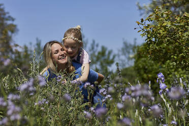 Happy mother carrying daughter piggyback in allotment garden - MCF00895