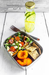 Lunchbox mit Rucolasalat mit bunten Tomaten, Mozzarella und Nüssen, Knäckebrot und Aprikosen und einer Flasche Wasser mit Zitronen und Limettenscheiben - SARF04590
