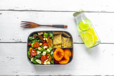 Lunchbox mit Rucolasalat mit bunten Tomaten, Mozzarella und Nüssen, Knäckebrot und Aprikosen und einer Flasche Wasser mit Zitronen und Limettenscheiben - SARF04591