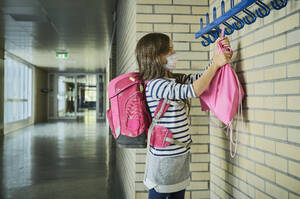 Girl wearing mask in school hanging up pouch - DIKF00502