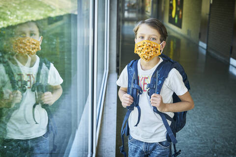 Junge mit Maske in der Schule, gespiegelt im Fenster, lizenzfreies Stockfoto