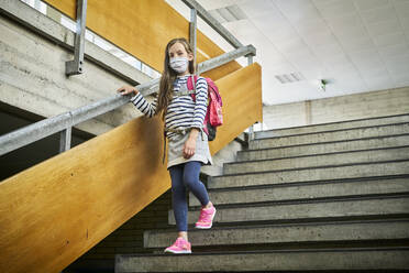 Girl wearing mask in school walking down stairs - DIKF00509