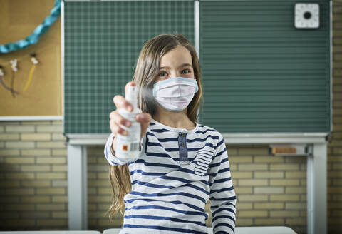 Portrait of girl wearing mask in classroom spraying sanitizer stock photo
