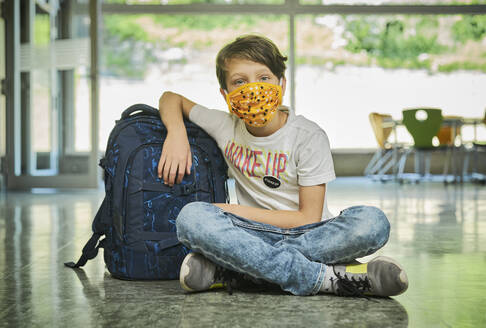 Boy sitting on the floor in school wearing mask - DIKF00518