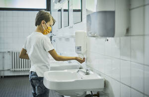 Boy wearing mask on school toilet washing his hands - DIKF00519