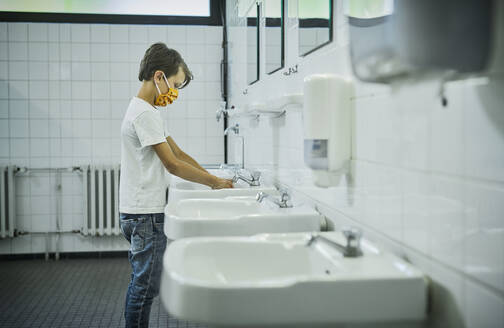 Boy wearing mask on school toilet washing his hands - DIKF00520