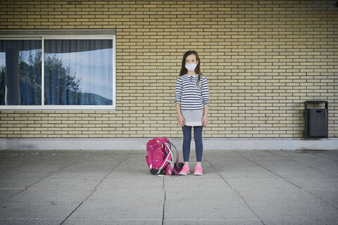 Girl with schoolbag wearing mask standing in front of building stock photo