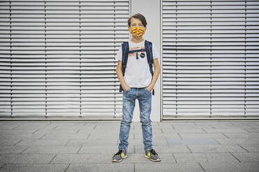 Junge mit Schultasche und Maske vor einem Gebäude stehend - DIKF00525