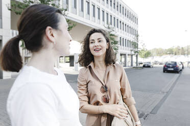 Glückliche Geschäftsfrauen unterhalten sich auf der Straße vor einem Bürogebäude - KMKF01394