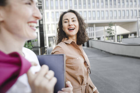 Glückliche Geschäftsfrau im Gespräch mit einem Kollegen, während sie gegen ein Bürogebäude läuft - KMKF01404