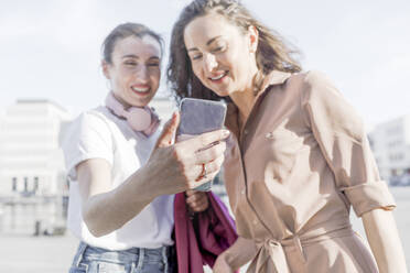 Glückliche Geschäftsfrauen benutzen ihr Smartphone an einem sonnigen Tag - KMKF01414