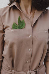 Businesswoman wearing brown overalls with leaves in pocket - KMKF01422