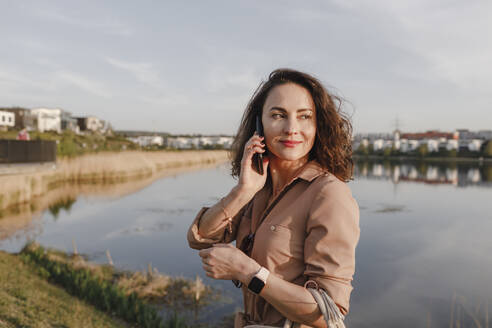 Schöne Geschäftsfrau schaut weg, während sie ihr Smartphone am Seeufer benutzt - KMKF01428