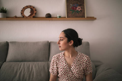 Nachdenkliche junge Frau sitzt zu Hause auf dem Sofa, lizenzfreies Stockfoto