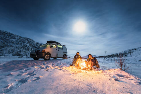 Campers at camp fire in winter landscape in polar night, Kilpisjaervi, Enontekioe, Finland - WVF01531