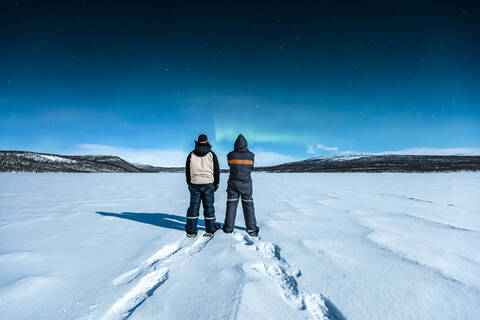 Snowshoe hikers standing in winter landscape watching northern lights above Ropijarvi, Ropinsalmi, Enontekioe, Finland stock photo