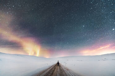 Mann auf Landstraße unter Sternenhimmel mit Nordlicht, Lebesby, Norwegen - WVF01619