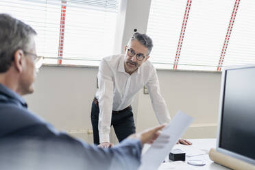 Gutaussehender Geschäftsmann diskutiert mit männlichem Fachmann am Schreibtisch im Büro - DIGF11273