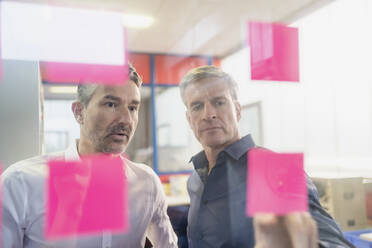 Mature businessmen discussing over adhesive notes on glass at office during meeting - DIGF11274