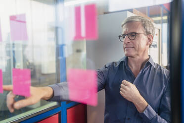 Reifer Geschäftsmann, der auf einen Klebezettel auf einem Glas zeigt, während er im Büro eine Strategie plant - DIGF11281