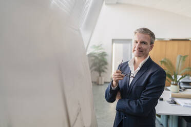 Portrait of smiling male entrepreneur holding eyeglasses while standing by whiteboard in office - DIGF11285