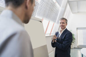 Lächelnder Geschäftsmann, der einen männlichen Mitarbeiter während einer Besprechung im Büro ansieht - DIGF11288