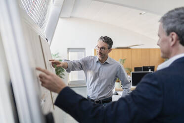 Mature male entrepreneur pointing while explaining strategy to businessman at office during meeting - DIGF11289