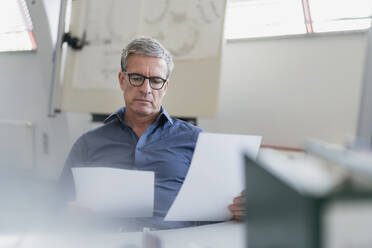 Handsome mature businessman reading papers while sitting at desk in office - DIGF11303