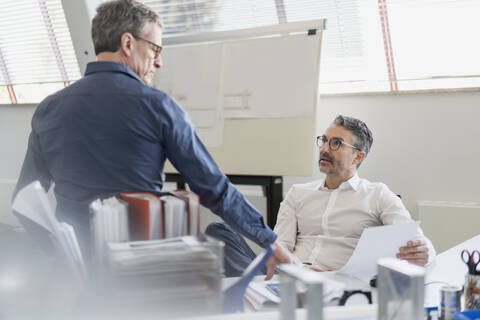 Reife Geschäftsleute, die im Büro sitzend über ein Dokument diskutieren, lizenzfreies Stockfoto