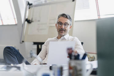 Gut aussehender Mann, der ein Dokument liest, während er am Schreibtisch im Büro sitzt - DIGF11310