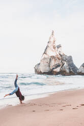 Woman performing handstand on shore at Ursa Beach, Lisboa Region, Portugal - FVSF00364