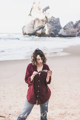 Young woman holding feather while standing at Ursa Beach, Lisboa Region, Portugal - FVSF00366