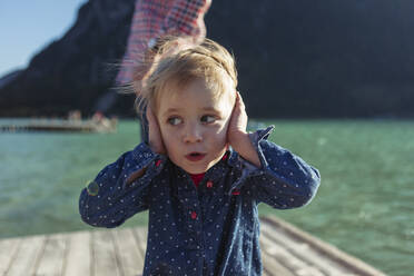Cute girl covering ears while father in background on boardwalk at Achensee, Tyrol State, Austria - JLOF00391