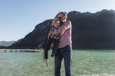Vater küsst, während er seinen Sohn gegen einen Berg am Achensee trägt, Bundesland Tirol, Österreich - JLOF00392