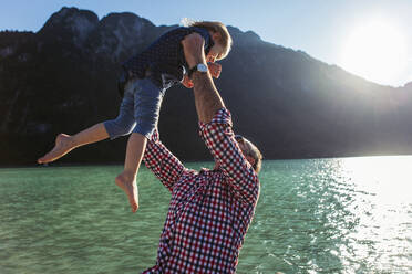 Vater hält seine Tochter hoch, während er vor einem Berg und einem See am Achensee steht, Bundesland Tirol, Österreich - JLOF00393