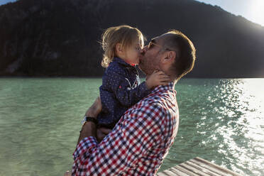 Vater und Tochter küssen sich vor einem Berg und einem See am Achensee, Bundesland Tirol, Österreich - JLOF00396