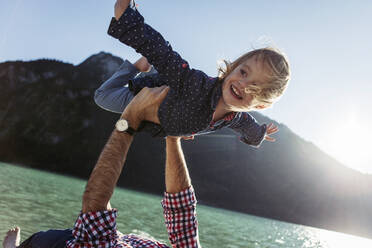 Happy girl with arms outstretched being carried by father at Achensee, Tyrol State, Austria - JLOF00407