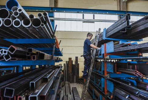 Man working with metal bars on a shelf in a factory - DIGF11344