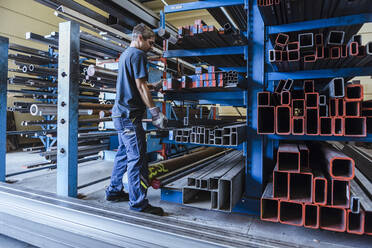 Man working with metal bars on a shelf in a factory - DIGF11346