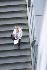 Geschäftsfrau, die ihr Smartphone benutzt, während sie eine Treppe in der Stadt hinuntergeht - DIGF11381